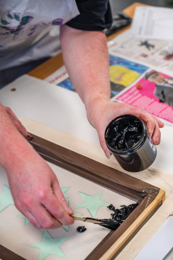 Photograph of hands applying ink to a printing screen