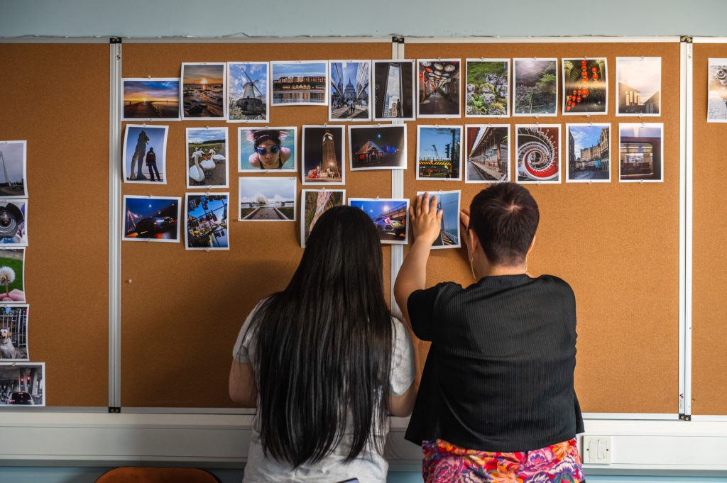 Photograph of two women pinning their photography portfolio images to a noticeboard