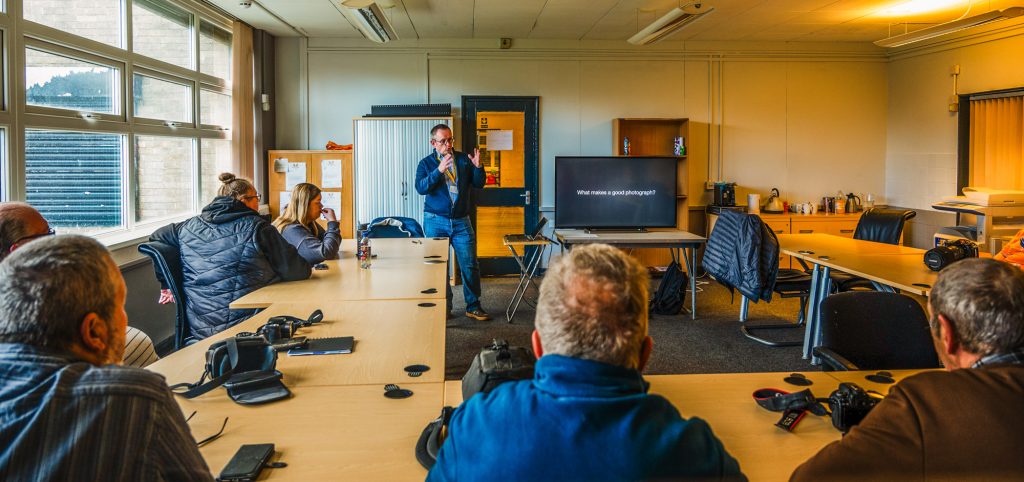 Photograph of a classroom setting with people sat at desks being taught by an instructor